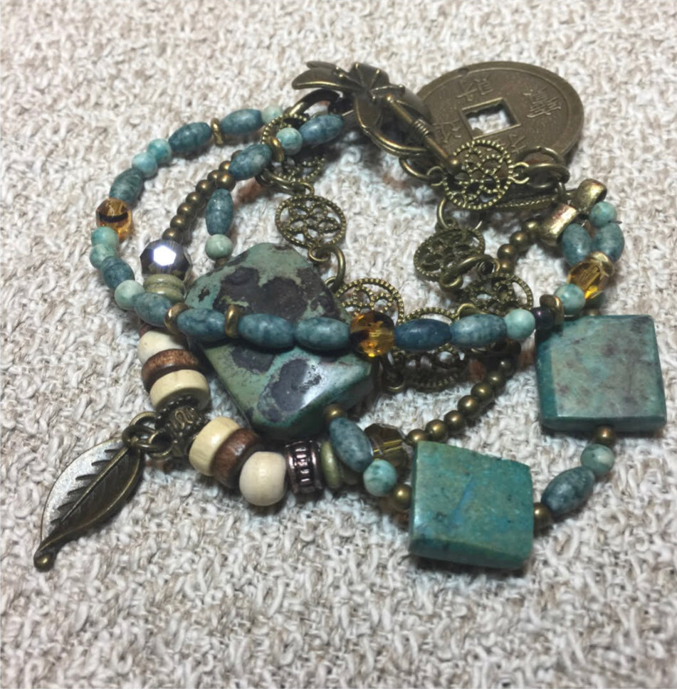 This bracelet with muted shades of turquoise, brown, and ivory is made of semi-precious stones, brass, bone and jade with a metal clasp is culturally inspired. 
